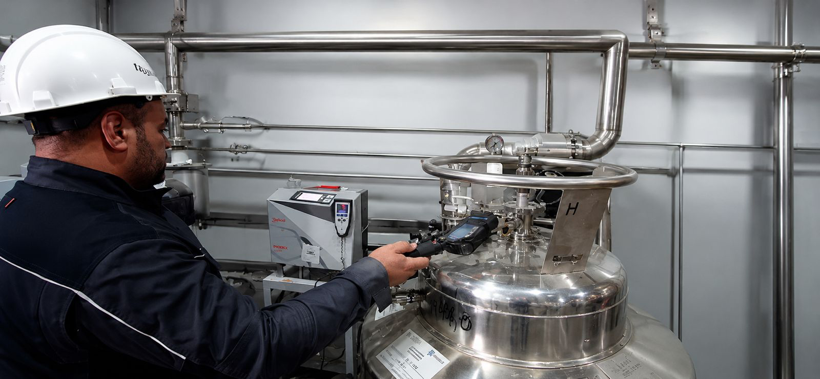Technician using a handheld instrument to examine valves on a cryogenic Dewar
